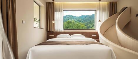A bedroom with a large bed, a view of a forest, and a curved wall.