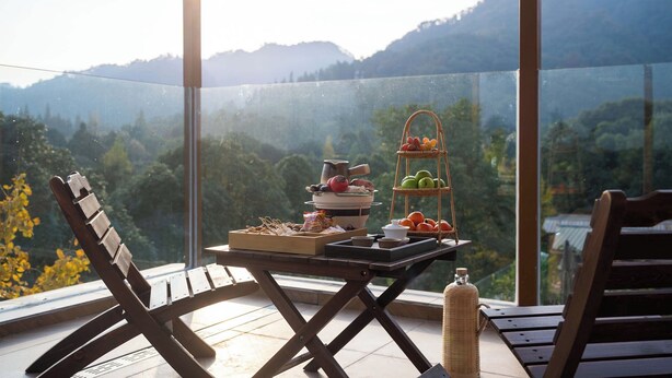 Un balcón con una mesa lista para el desayuno, una cesta de mimbre y una botella.