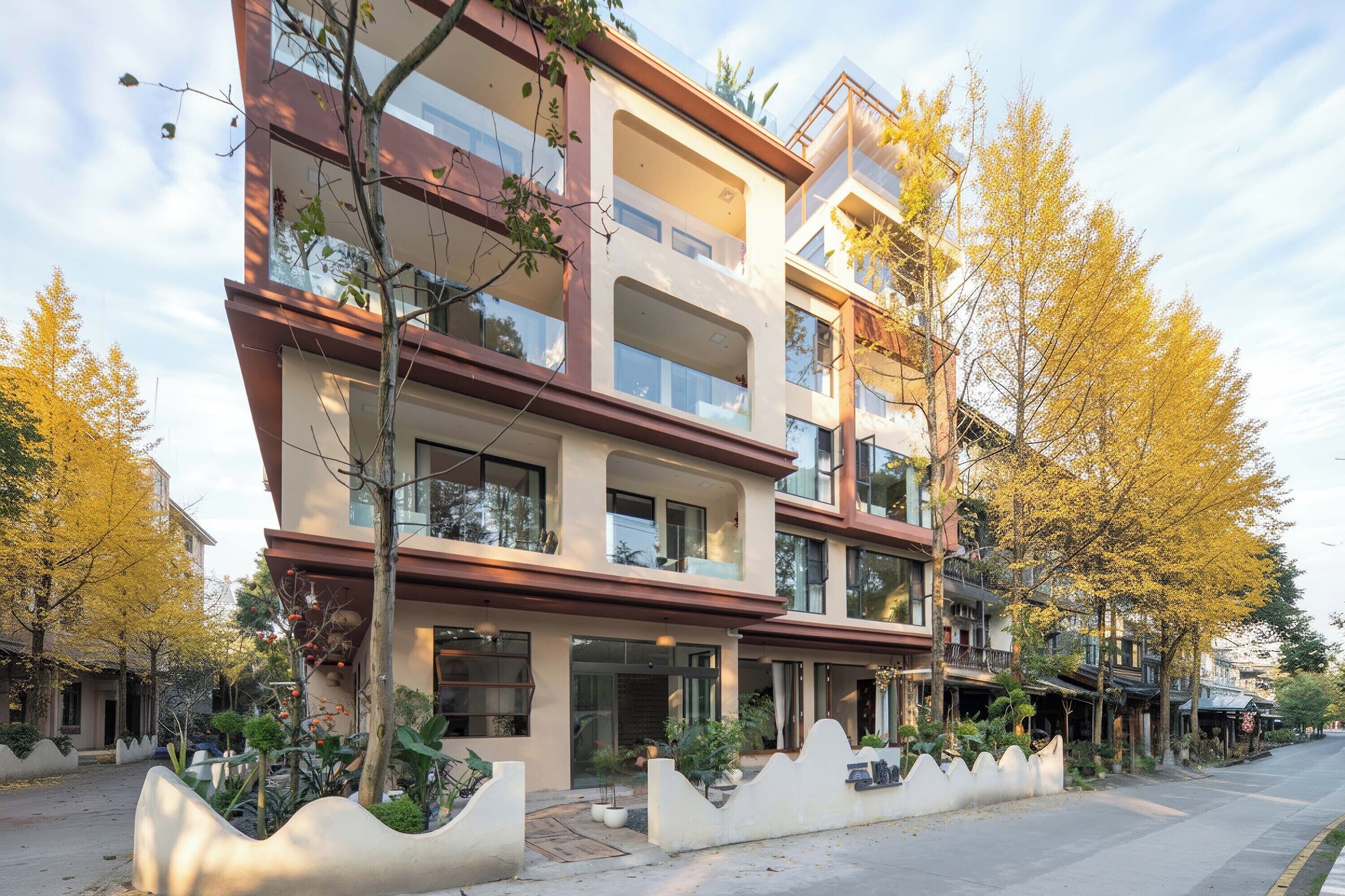 A multi-story building with balconies, a central entrance, and surrounding greenery.