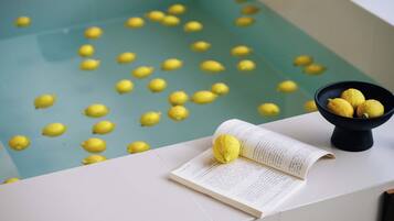 Une baignoire avec des pastilles de bain jaunes, un bol de citrons et un livre ouvert sur une surface blanche.