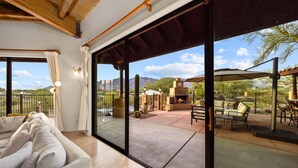 Un moderno salón con un amplio ventanal corredera que da a un patio exterior con una chimenea y asientos.