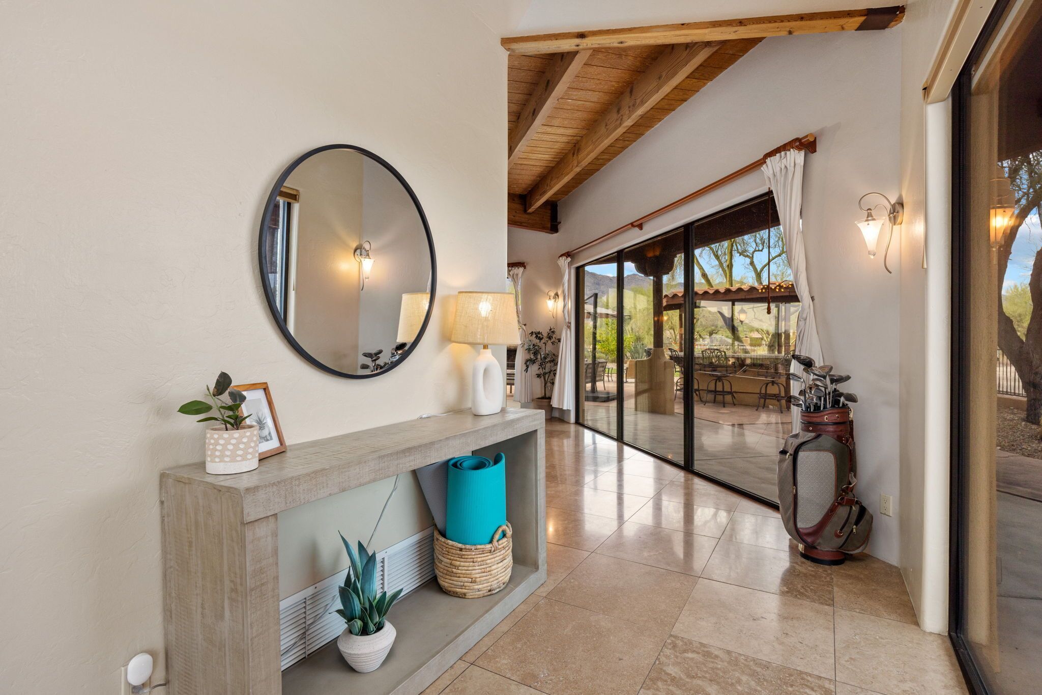 A modern interior with a wooden console table, a round mirror, and a glass door leading to an outdoor patio.