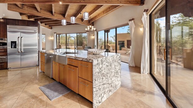 Una cocina moderna con una isla grande, electrodomésticos de acero inoxidable, armarios de madera y un techo alto con vigas a la vista.