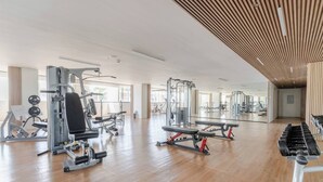 Ein großzügiger Fitnessraum mit unterschiedlichen Trainingsgeräten, großen Fenstern und einer Holzzieldecke.
