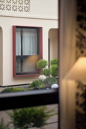 A window with a red frame and a curtain, a small tree, and a decorative wall panel.