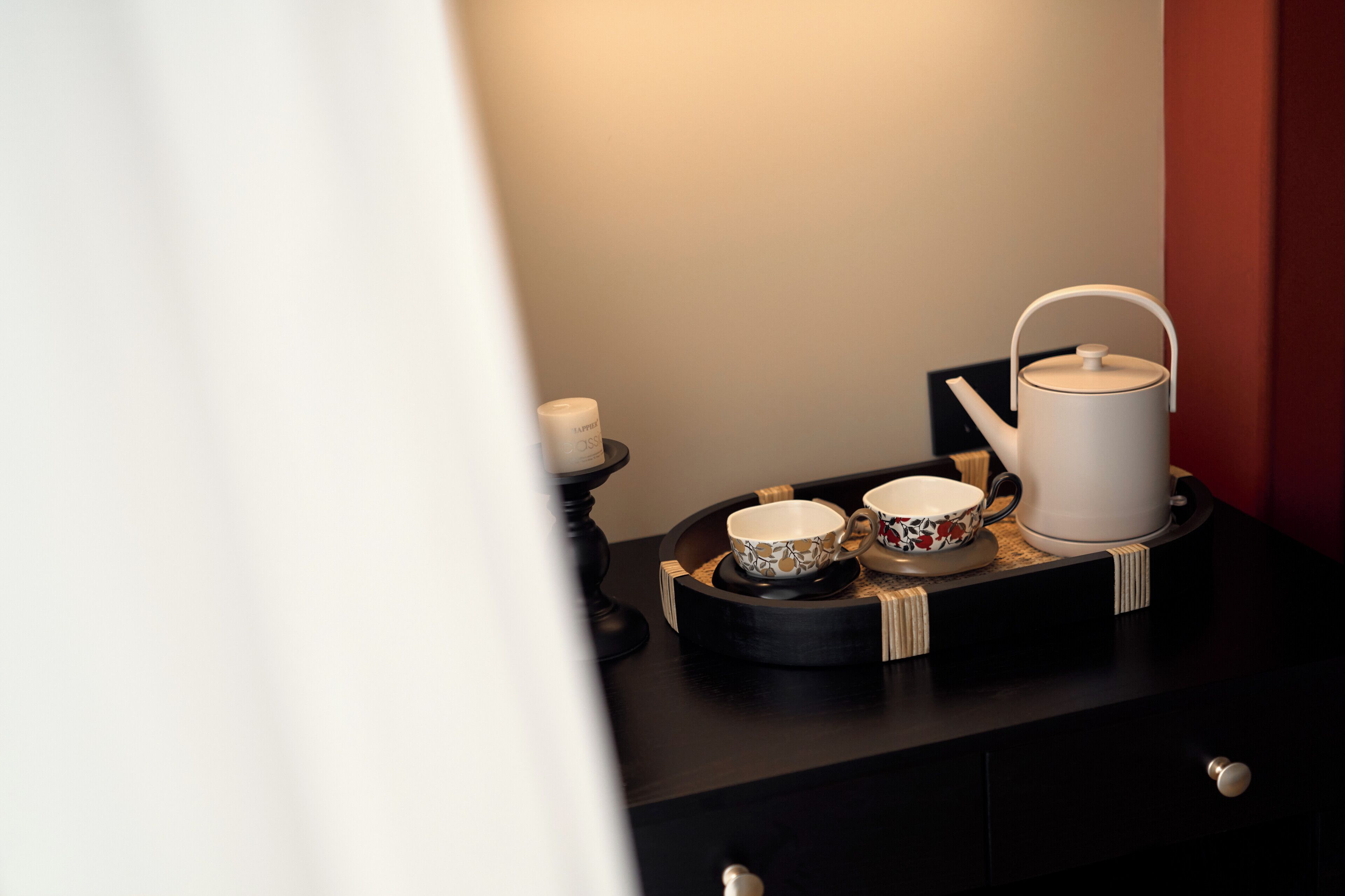 Un plateau sur lequel se trouvent une théière, des tasses et une bougie, le tout posé sur une surface sombre.