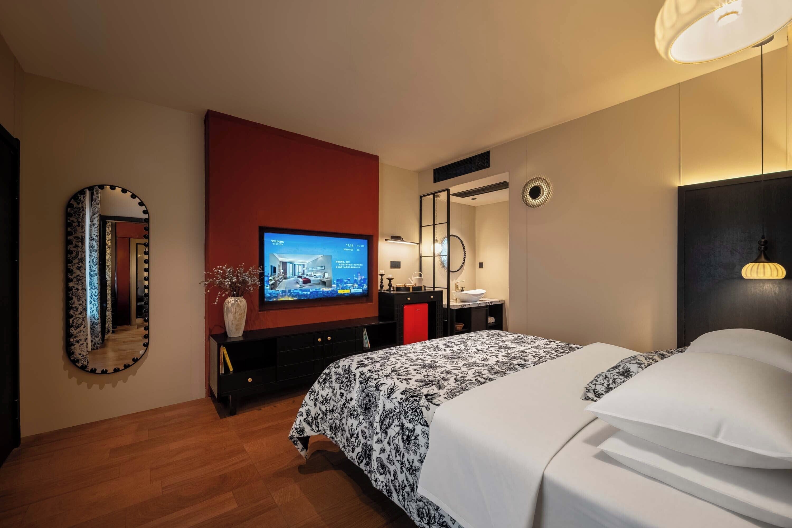 Ein Hotelzimmer mit Bett, Fernseher, Spiegel, einer roten Akzentwand und Holzboden.