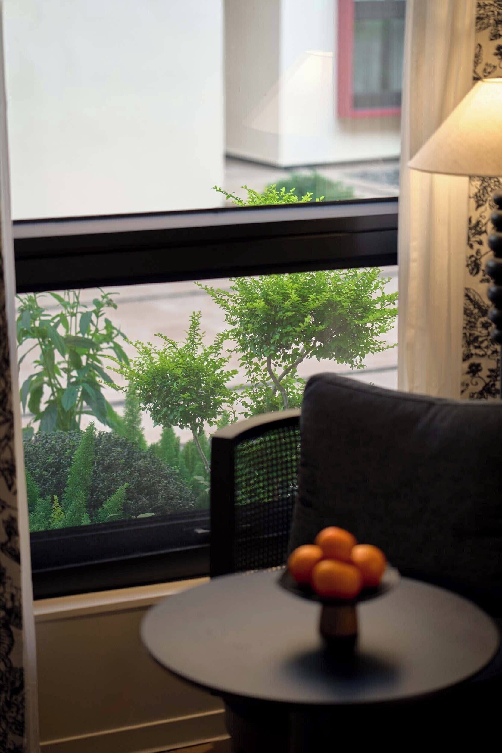 A room with a window, a small round table with a fruit bowl, and a chair.
