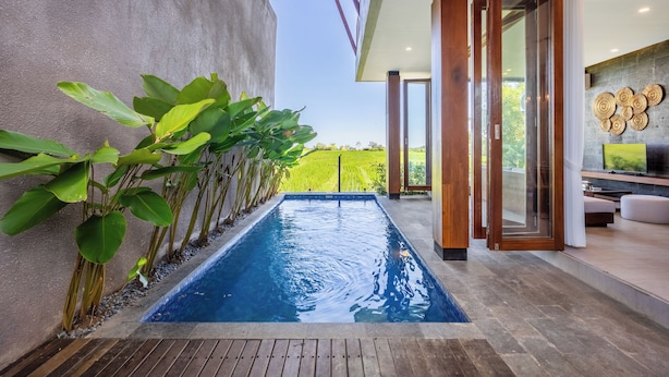 A swimming pool with a view of a green landscape, a modern interior with a wooden floor, and a glass door leading to a seating area. - Bhiseka Villa Kedungu by Aishwarya Bali (Tabanan)