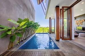 Ein Schwimmbad mit Blick auf eine grüne Landschaft, ein modernes Interieur mit Holzboden und eine Glastür zu einem Sitzbereich.