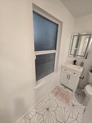 Un baño con ventana, lavamanos, espejo y retrete.