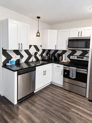 A modern kitchen with white cabinets, a black countertop, a stainless steel dishwasher, a microwave, and an oven. - Spacious 2BR/2BA Home in EaDo Houston – Full Kitchen, W/D, Near Downtown (Houston)