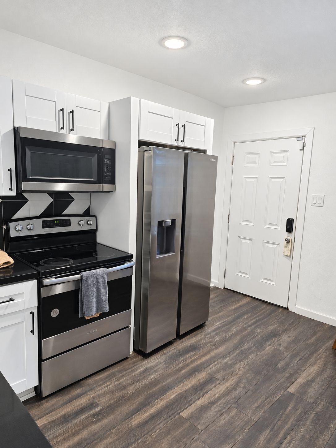 A modern kitchen with stainless steel appliances, white cabinetry, and a wooden floor.