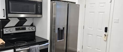 A modern kitchen with stainless steel appliances, white cabinetry, and a wooden floor.