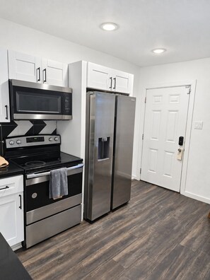 A modern kitchen with stainless steel appliances, white cabinetry, and a wooden floor. - Spacious 2BR/2BA Home in EaDo Houston – Full Kitchen, W/D, Near Downtown (Houston)