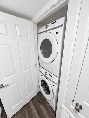 A laundry room with a stacked washer and dryer, white doors, and a wooden floor. - Spacious 2BR/2BA Home in EaDo Houston – Full Kitchen, W/D, Near Downtown (Houston)