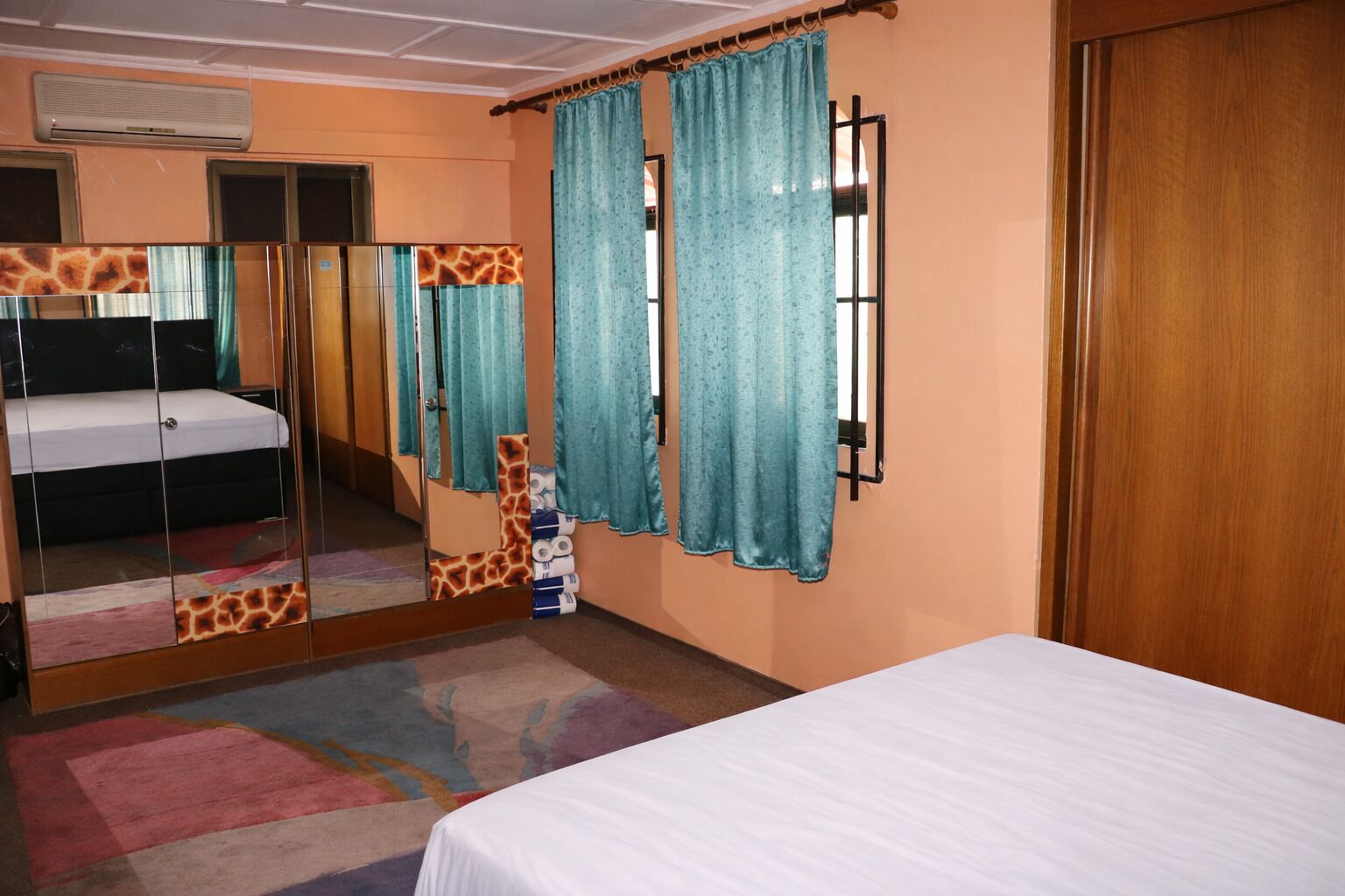 A hotel room with a bed, a mirror with giraffe patterns, a window with curtains, and a wooden door.