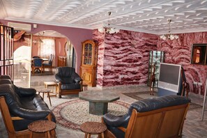 A living room with a sofa, armchairs, a coffee table, a TV, and a patterned wall. - Rico Home Stay (Nsawam)