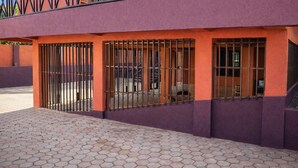 Un bâtiment à la façade violette, doté de fenêtres grillagées et d’un trottoir dallé.