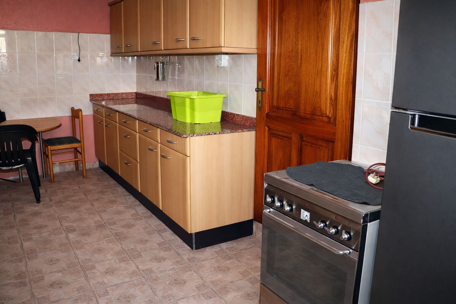 Een keuken met houten kastjes, een fornuis en een groene prullenbak.