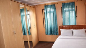 Une chambre à coucher avec un lit, une armoire et deux fenêtres avec des rideaux.