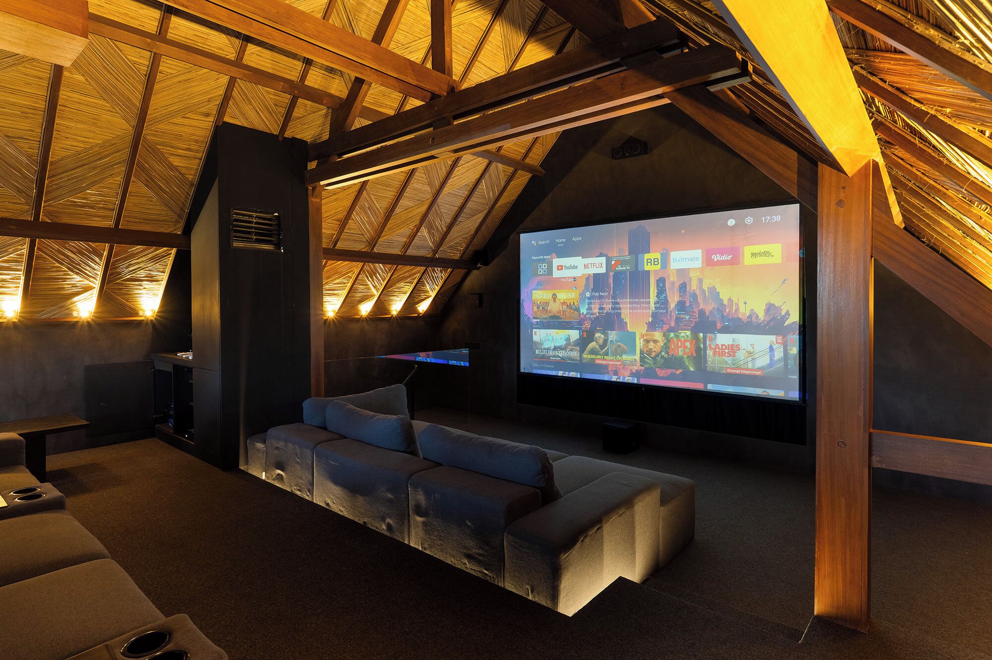 A cozy room with a sloped ceiling, a large screen for entertainment, a comfortable seating area, and a small table.