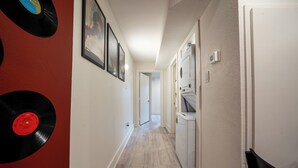 Un corridoio con pavimento in legno, una porta bianca e un frigorifero.