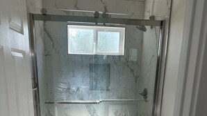 Kylpyhuone, jossa on lasiseinällä varustettu suihku, wc ja pesuallas.