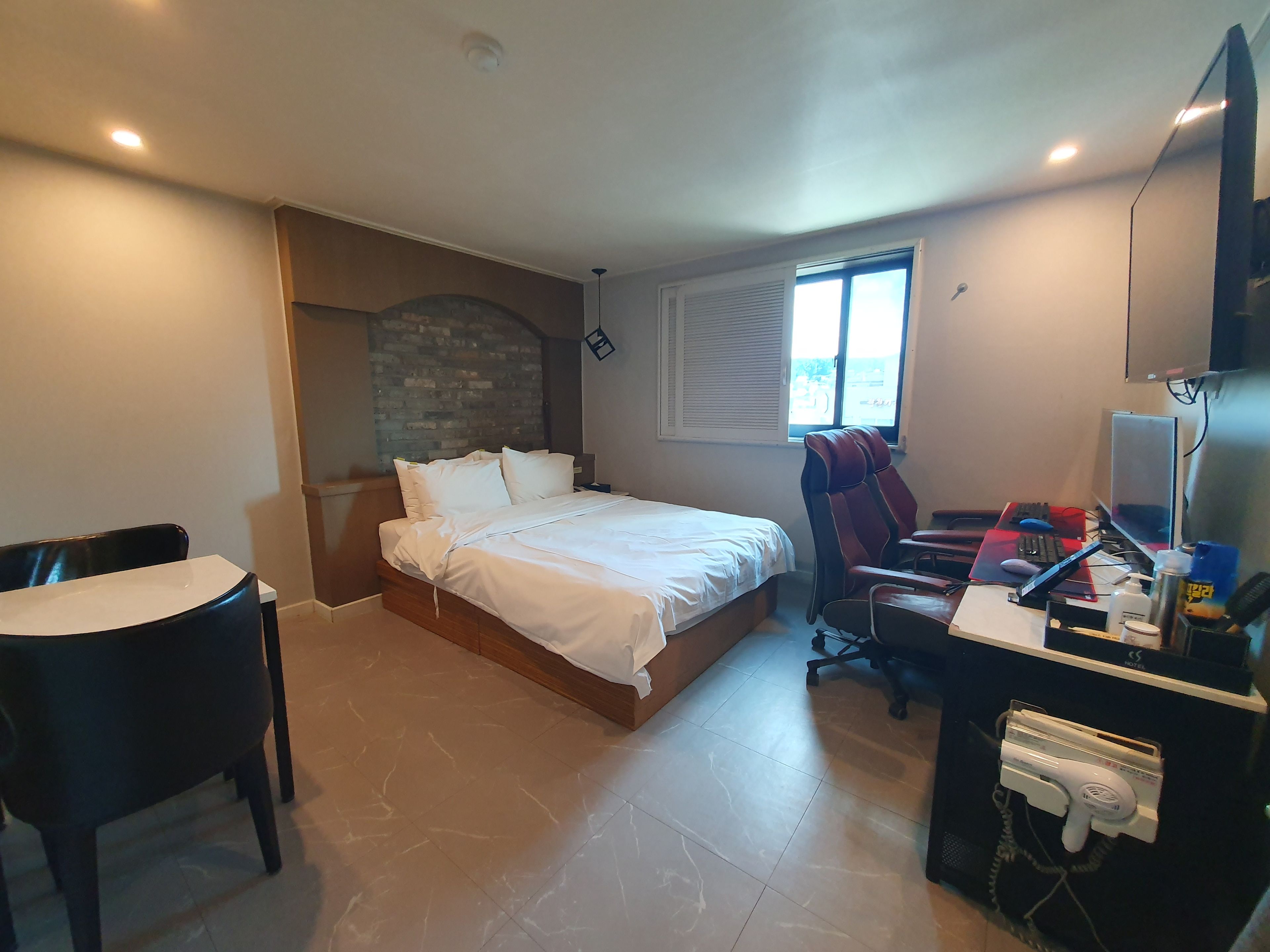 Una habitación de hotel con una cama, un escritorio con computadora, una silla y un ventanal.