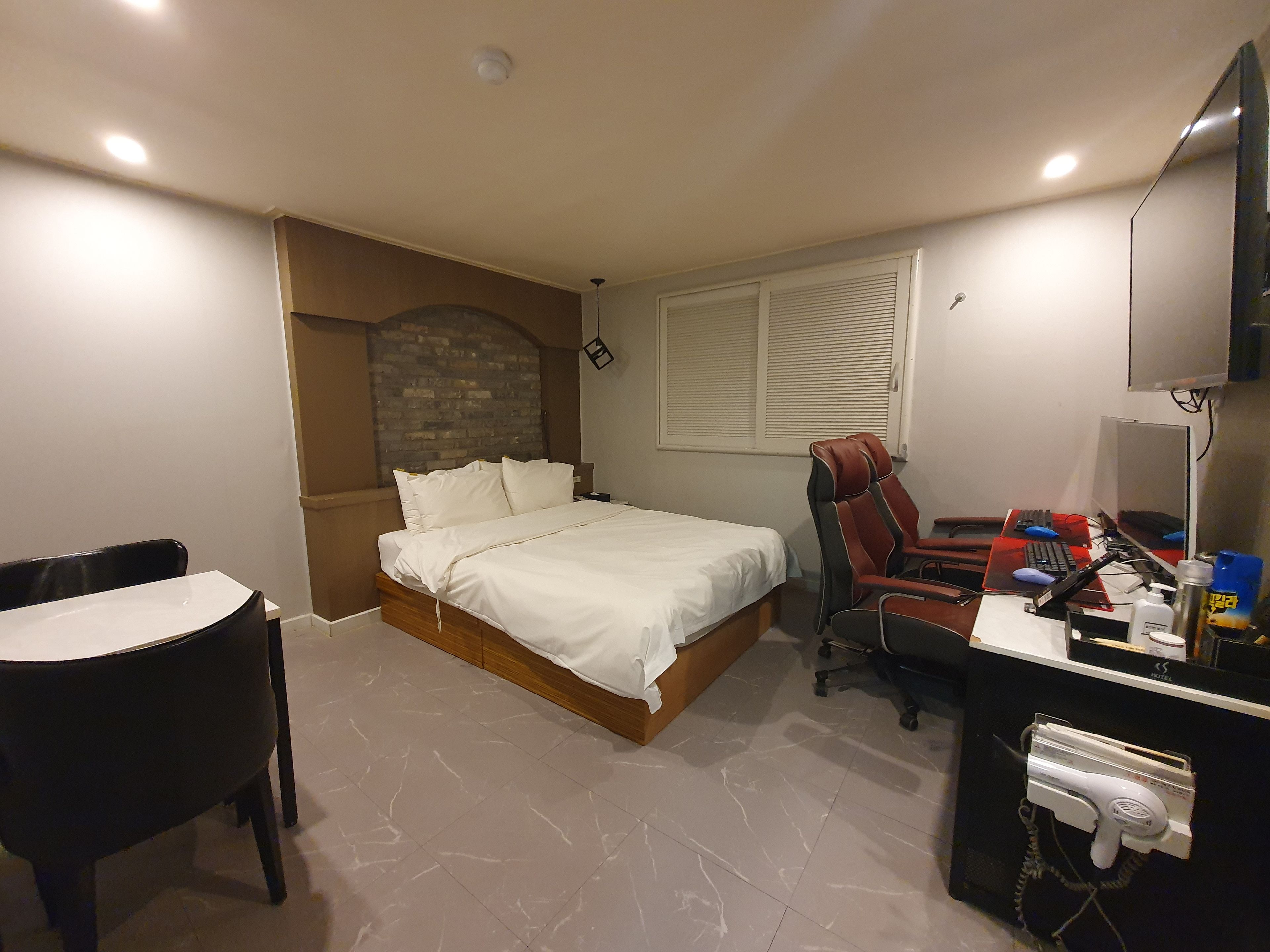 Habitación de hotel con cama, escritorio con computadora, silla y secador de pelo.