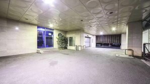 Un espacio interior con piso de baldosas, puerta de vidrio, una planta en maceta y baranda metálica.