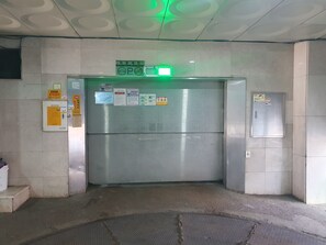 An elevator with a green exit sign, a metal door, and various informational notices on the wall.