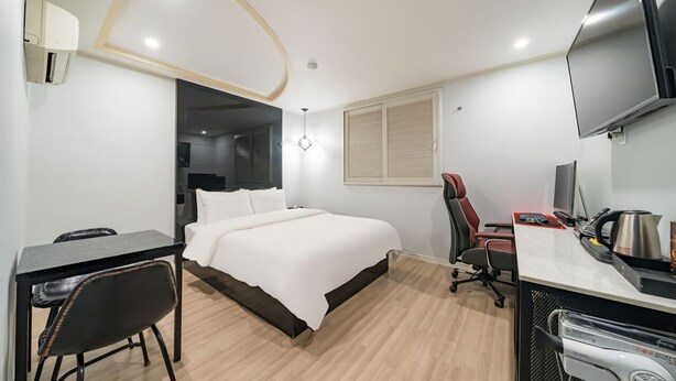 Una habitación de hotel con cama, escritorio, silla, televisor y equipo de ejercicio.