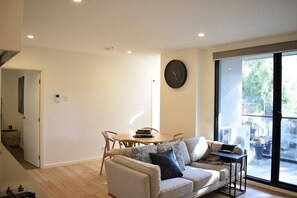 A modern living room with a sofa, a round table with books, a clock on the wall, and a large window. - Charming 2BDR Apartment in Richmond close to MCG (Richmond)