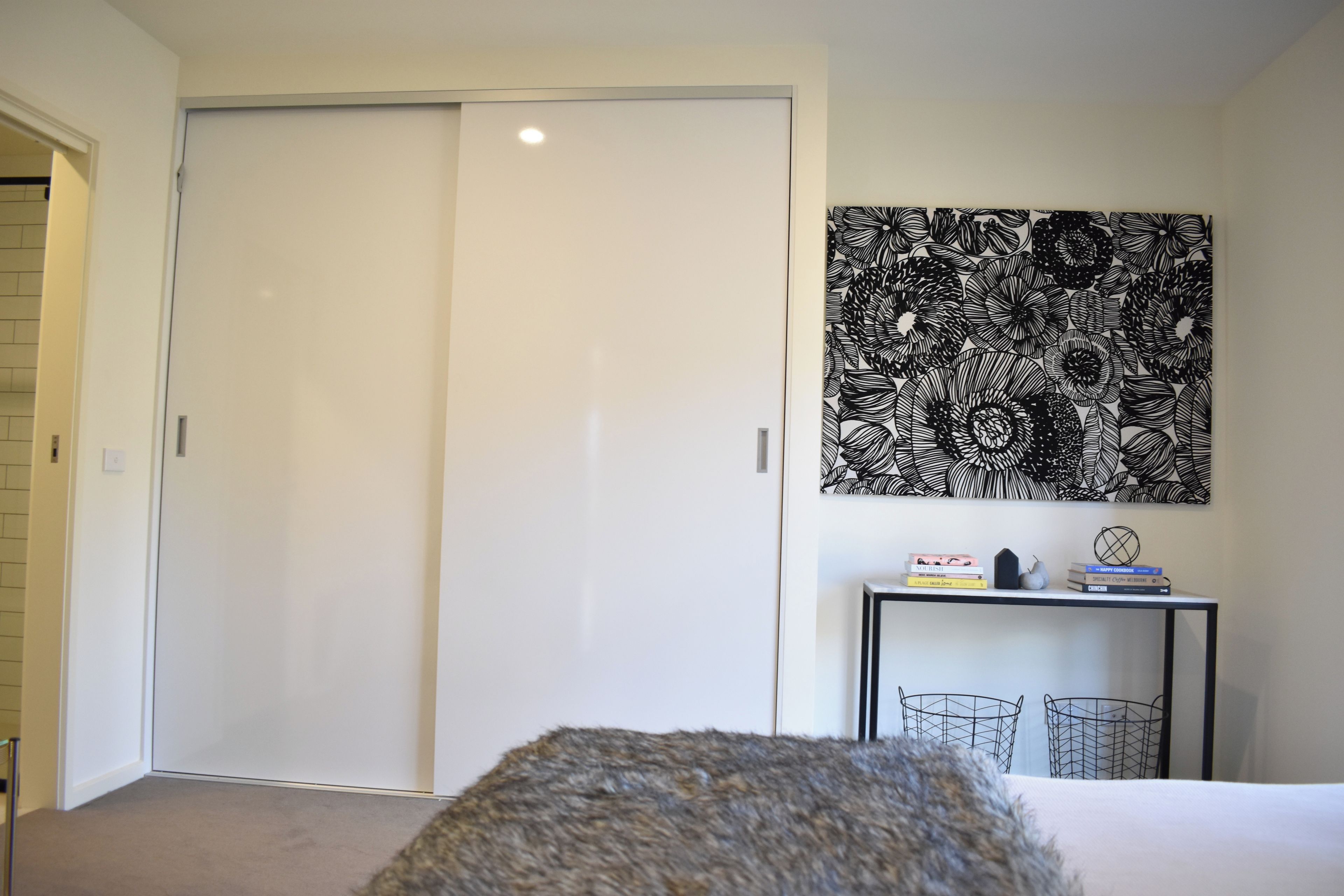 Ein Schlafzimmer mit geschlossener Tür, einem Wandbild, einem Nachttisch mit Büchern und einem Bett.