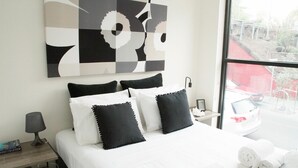 Une chambre d’hôtel avec un lit, des oreillers, une table de chevet, une lampe et une fenêtre donnant sur l’extérieur.