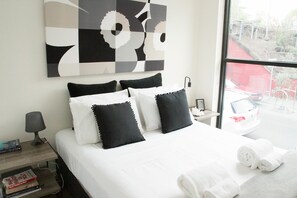 A hotel room with a bed, pillows, a nightstand, a lamp, and a window with a view of the outside. - Charming 2BDR Apartment in Richmond close to MCG (Richmond)