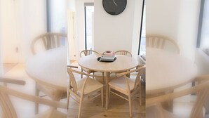 Une table de salle à manger ronde en bois, entourée de six chaises, une horloge au mur et une porte donnant sur une autre pièce.