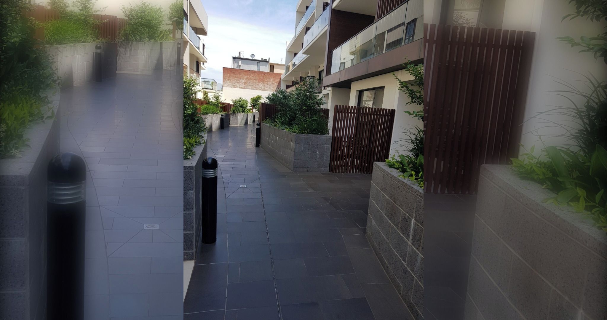 Un estrecho sendero urbano bordeado por edificios modernos con balcones, un acceso con reja y un bolardo de metal.