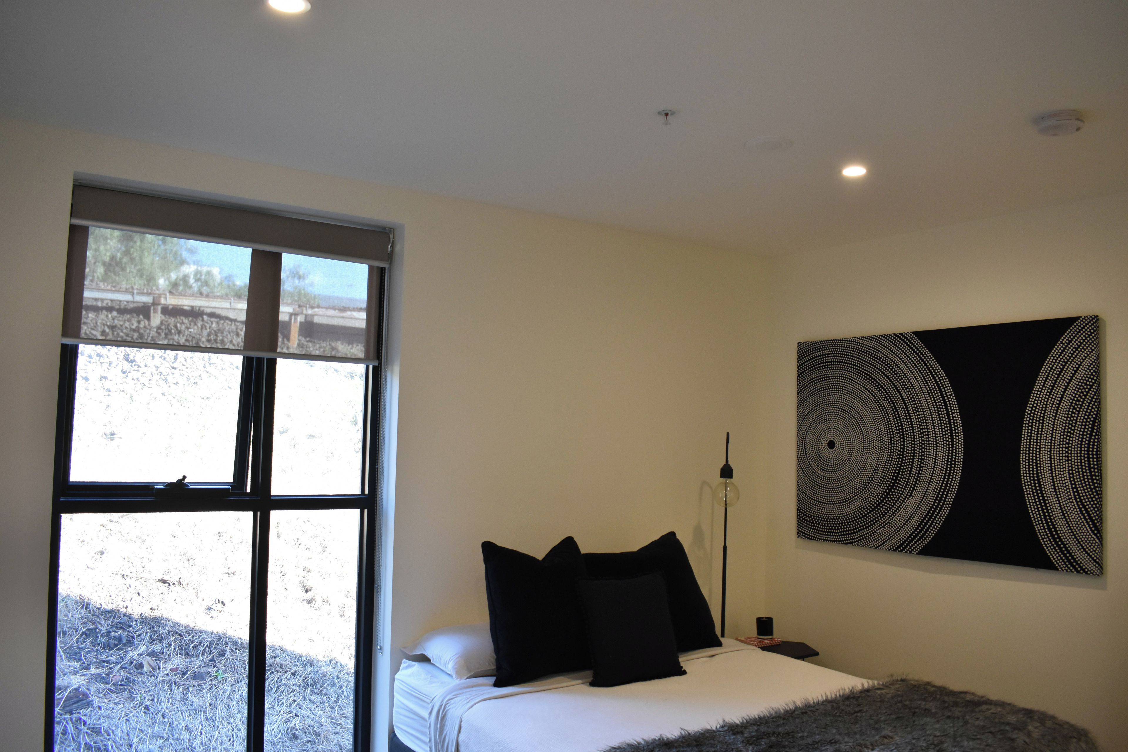Een slaapkamer met een bed, kussens, een lamp en een groot abstract schilderij aan de muur.
