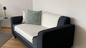 A dark-colored sofa with a white cushion and a green pillow against a textured wall. - Haus Saturn Studio STUDIO by Interhome (Saas-Grund)