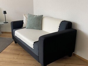 Ein dunkelbraunes Sofa mit einem weißen Kissen und einem grünen Kopfkissen vor einer strukturierten Wand.