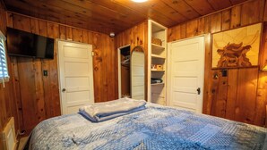 A wooden-paneled room with a bed, a television, and a mirror.