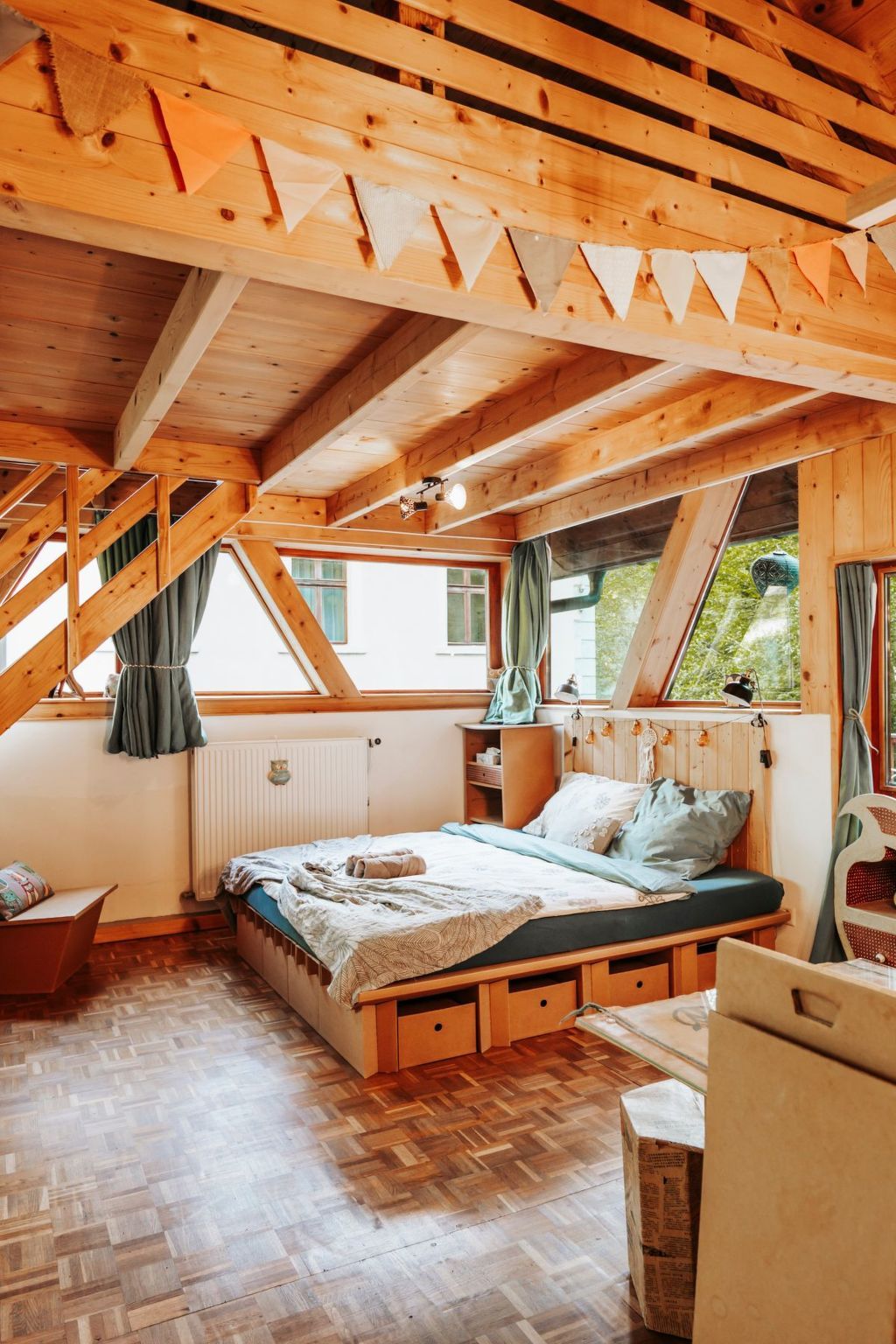 A cozy bedroom with a wooden ceiling, a bed with a blue mattress, a wooden dresser, and a window with curtains.