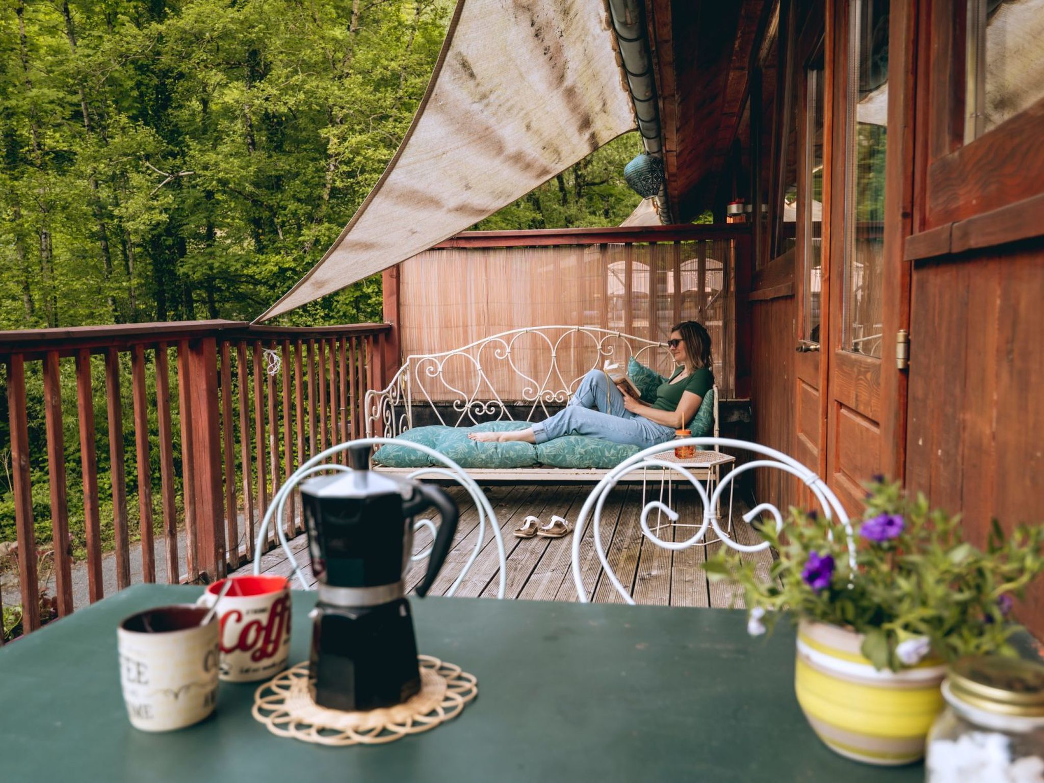 A person relaxing on a metal bed on a wooden deck with a table in the foreground.