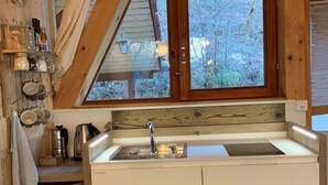 Cocina pequeña con ventana, vigas de madera y un lavamanos blanco.