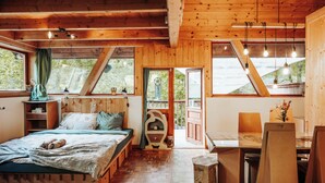 Una cabaña acogedora con una cama, un escritorio y una silla, paredes de madera y ventanas amplias.