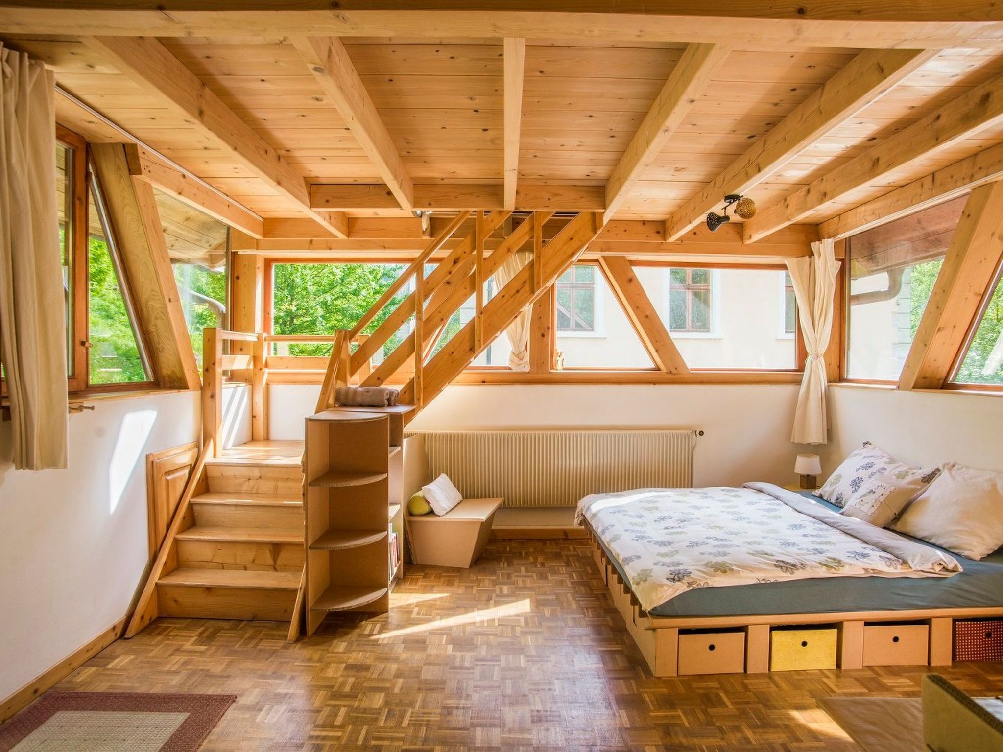 Quarto com escada de madeira, cama, radiador e janelas amplas.