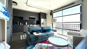Ein kompakter Wohnraum mit Küchenzeile, einer Couch, einem kleinen Tisch und einem großen Fenster mit Blick.