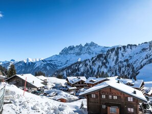 A snow-covered mountain village with wooden buildings, a ski lift, and a clear view of the mountains.